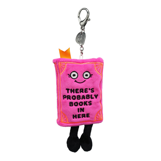 Pink book plush bag charm with "THERE'S PROBABLY BOOKS IN HERE" embroidered messaging, smiling face, dangling legs, and silver lobster-clasp keychain attachment