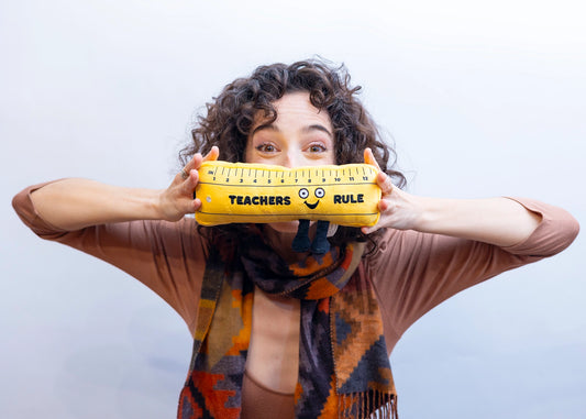 Smiling teacher holding soft yellow Teachers Rule Plush Ruler in front of her face — a cute novelty plush toy gift